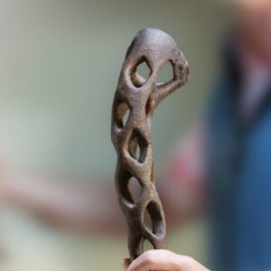 Handle of a journey stick; a carved staff gifted to couples on a wedding day. This journey stick has a flute handle that is hollowed out and marked using a burning tool, giving the handle a textured dark finish.