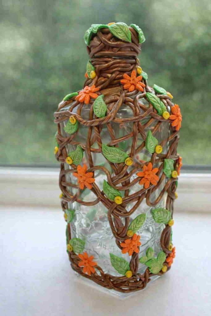 Large gin style clear glass bottle dressed in brown polymer vines with small green leaves and orange flowers