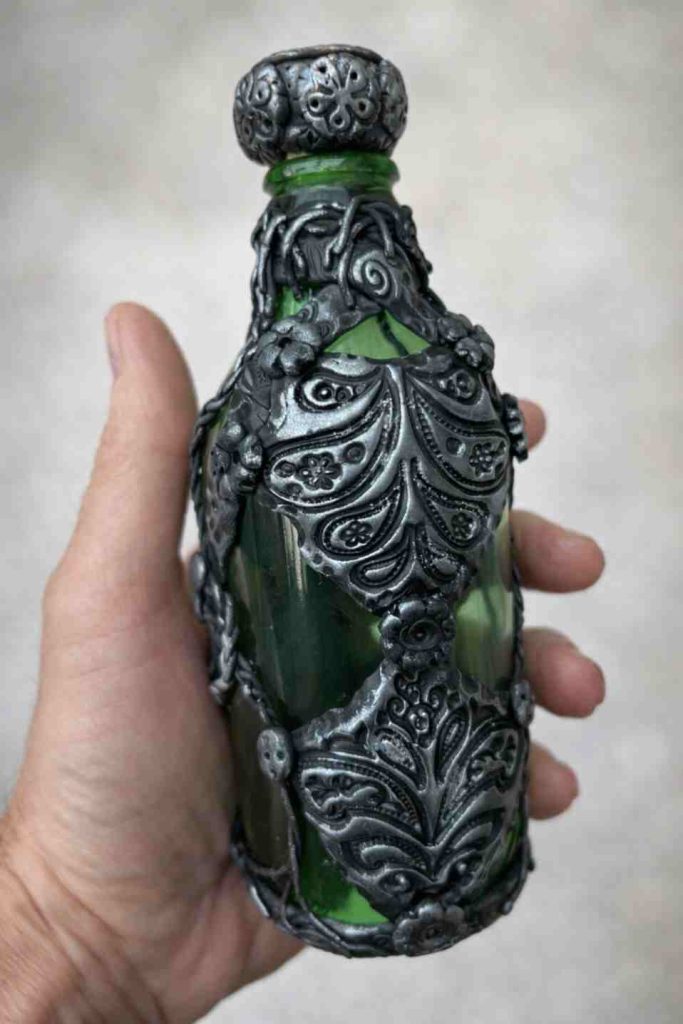 Small green beer bottle dressed in pewter effect polymer clay in the style of medieval genie bottle