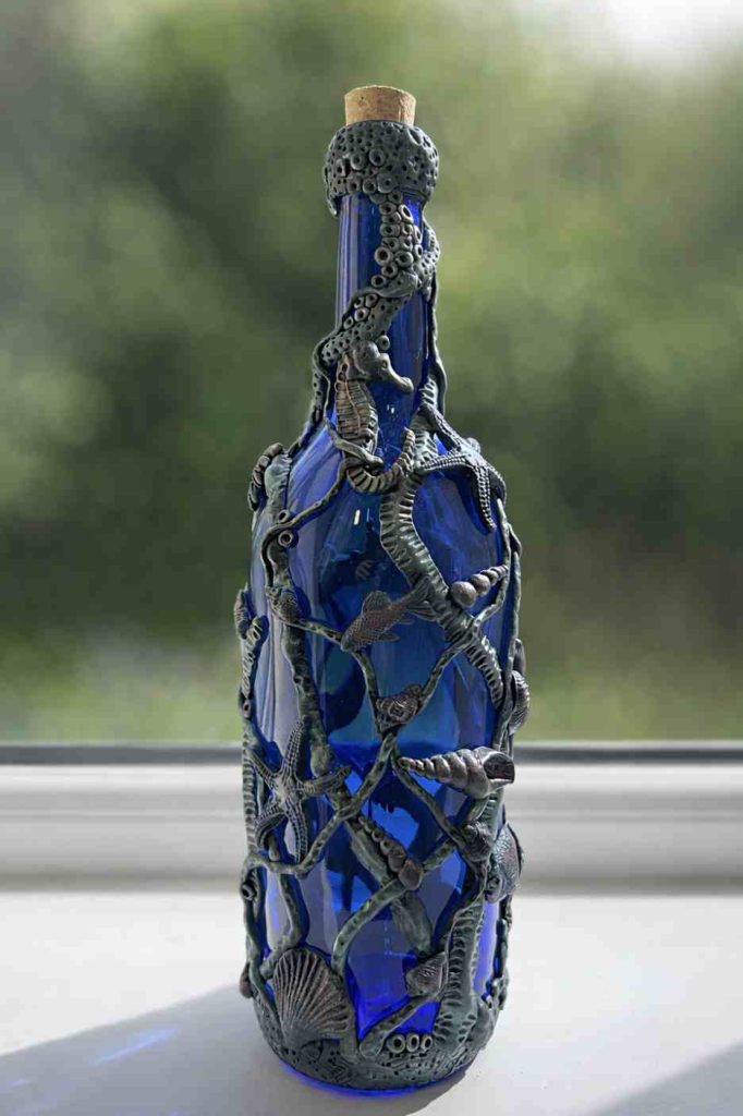 Tall blue bottle dressed in sea-themed polymer clay with shells, sea creatures and weeds