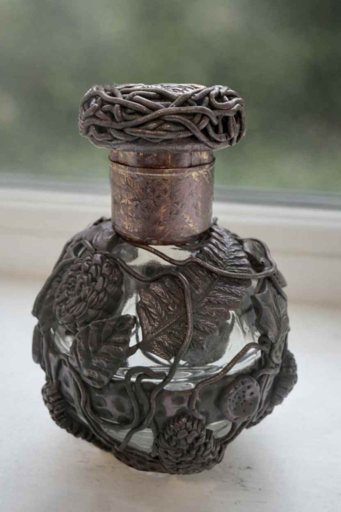 small rounded perfume style bottle wrapped in a wire cage with polymer clay leaf motifs, bronze coloured