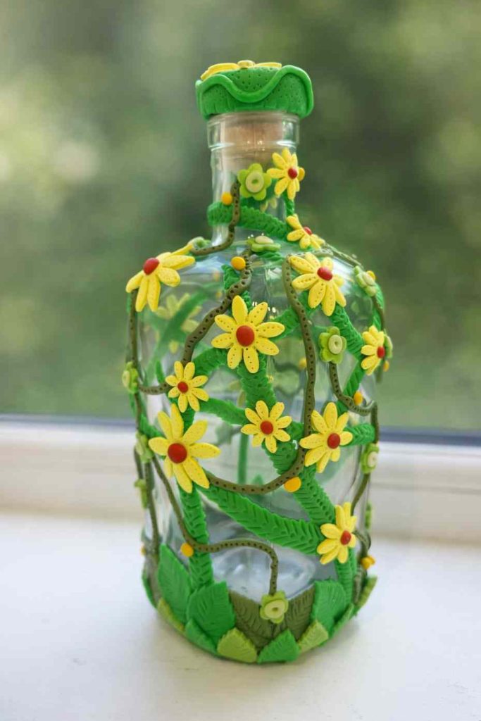 large gin style clear glass bottle dressed in lush green polymer vines, yellow flowers and orange buds